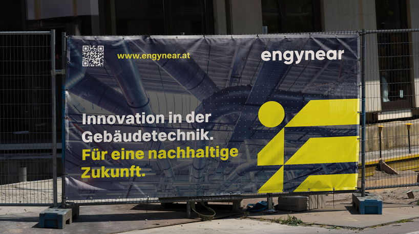 Bauzaun mit dunklem Werbebanner für Engynear Gebäudetechnik