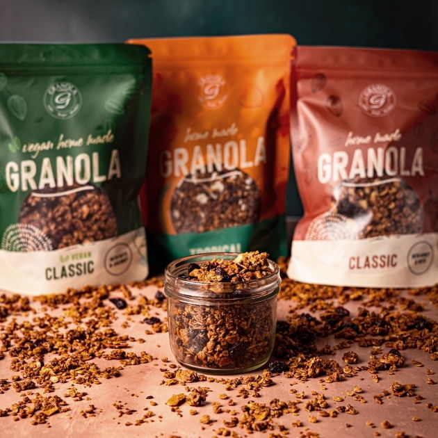 Drei Packungen Müsli der Granola Company auf beigem Untergrund