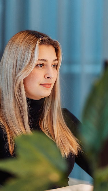 Eine junge, blonde Frau sitzt konzentriert an einem modernen Büroarbeitsplatz und blickt auf ihren PC-Bildschirm