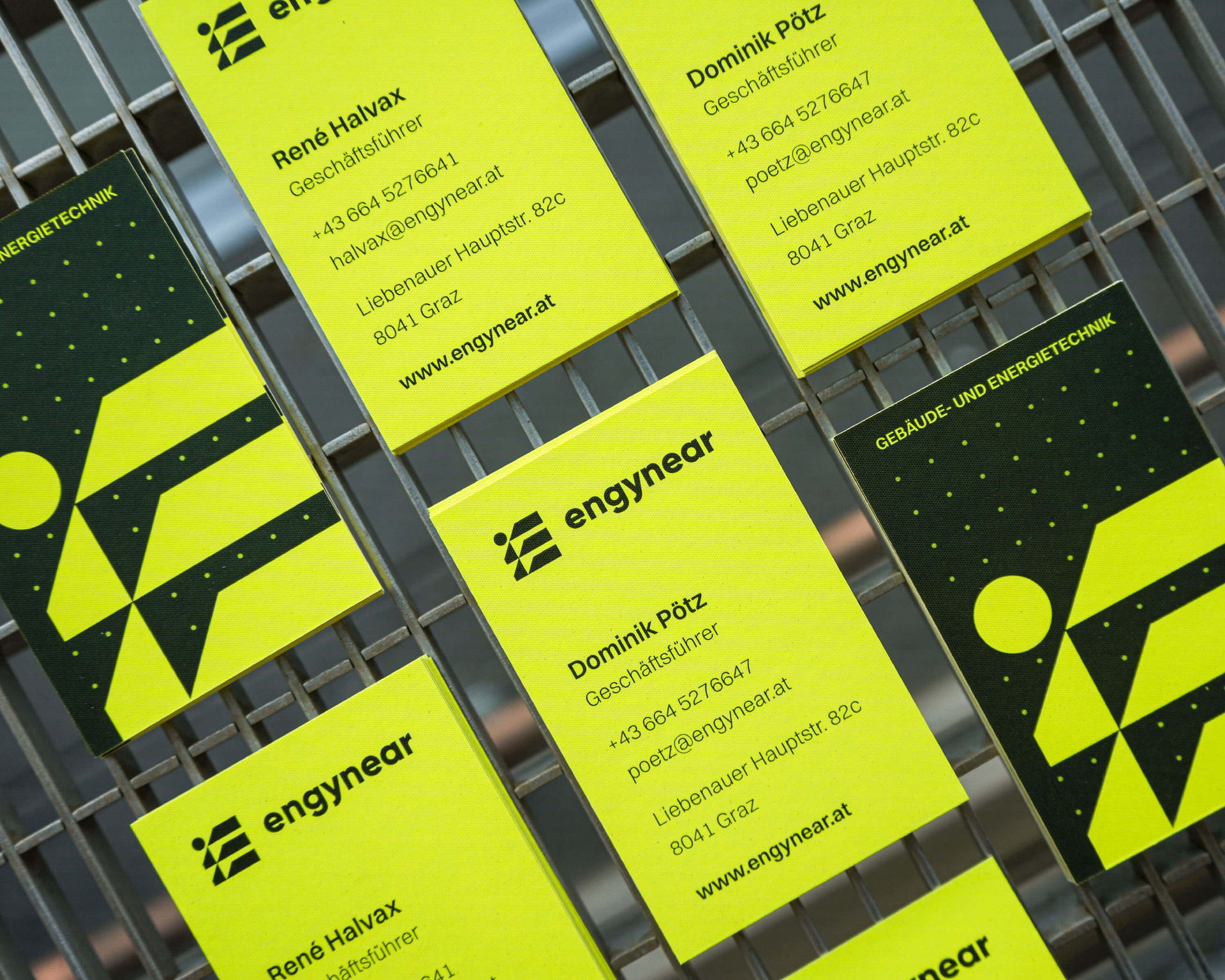 Visitenkarten von Engynear mit leuchtend gelber Seite und dunkler Rückseite auf industriellem Background