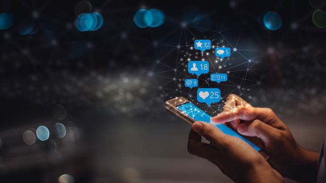 Nahaufnahme von Händen, die ein Smartphone bedienen. Über dem Display schweben Social-Media-Symbole wie Likes, Nachrichten und Follower-Zahlen, verbunden durch ein Netzwerk aus leuchtenden Linien auf dunklem Hintergrund.