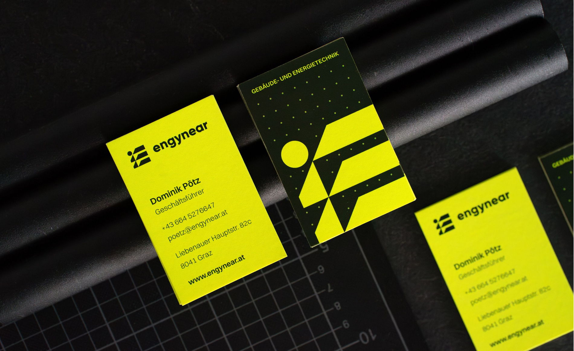 Visitenkarten von Engynear mit leuchtend gelber Seite und dunkler Rückseite auf industriellem Background