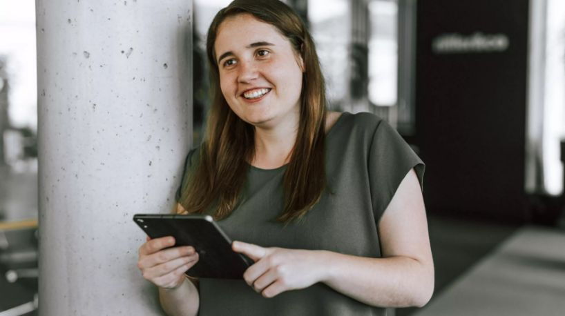 Katharina mit iPad in der Hand grinst an der Kamera vorbei